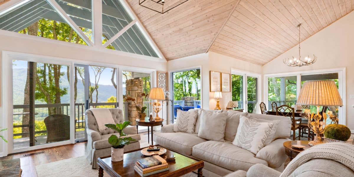 Spacious living room with vaulted wooden ceiling, large windows offering a mountain view, and comfortable seating.